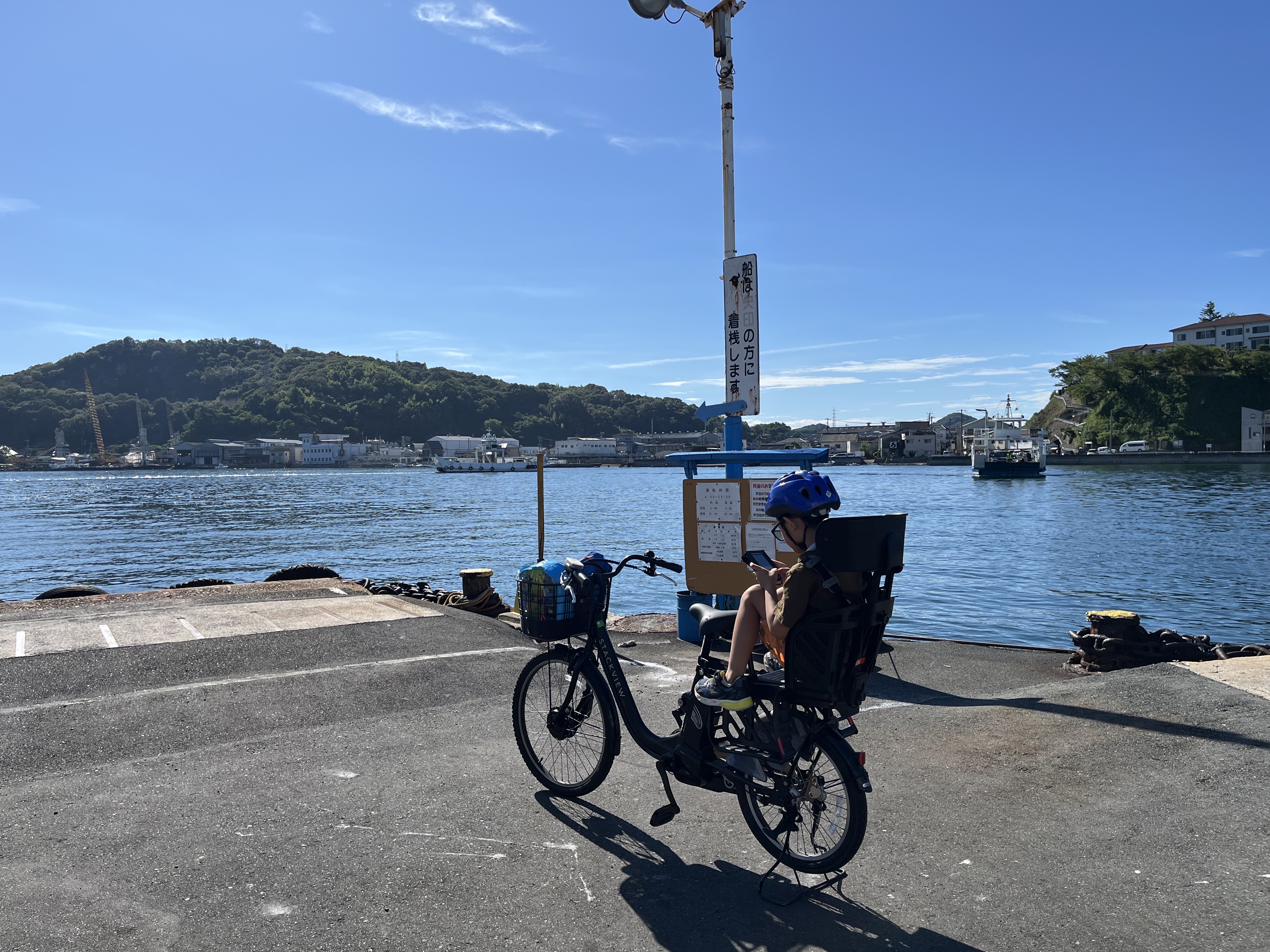 A child on a bicycle looking at a handheld by the harbour